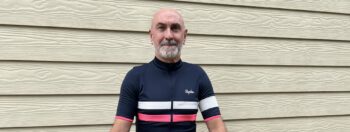 Our CEO, Tony Summers, standing in front of a wooden building in his cycling top.