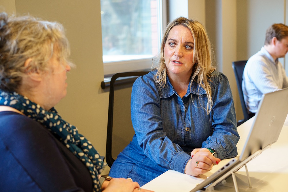 Two women chatting at a desk with a laptop