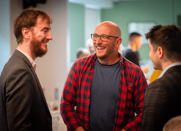 Three men stood together chatting and smiling
